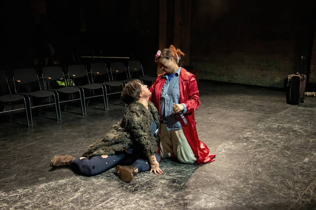Two actors kneel and look toward each other in mid-performance.
